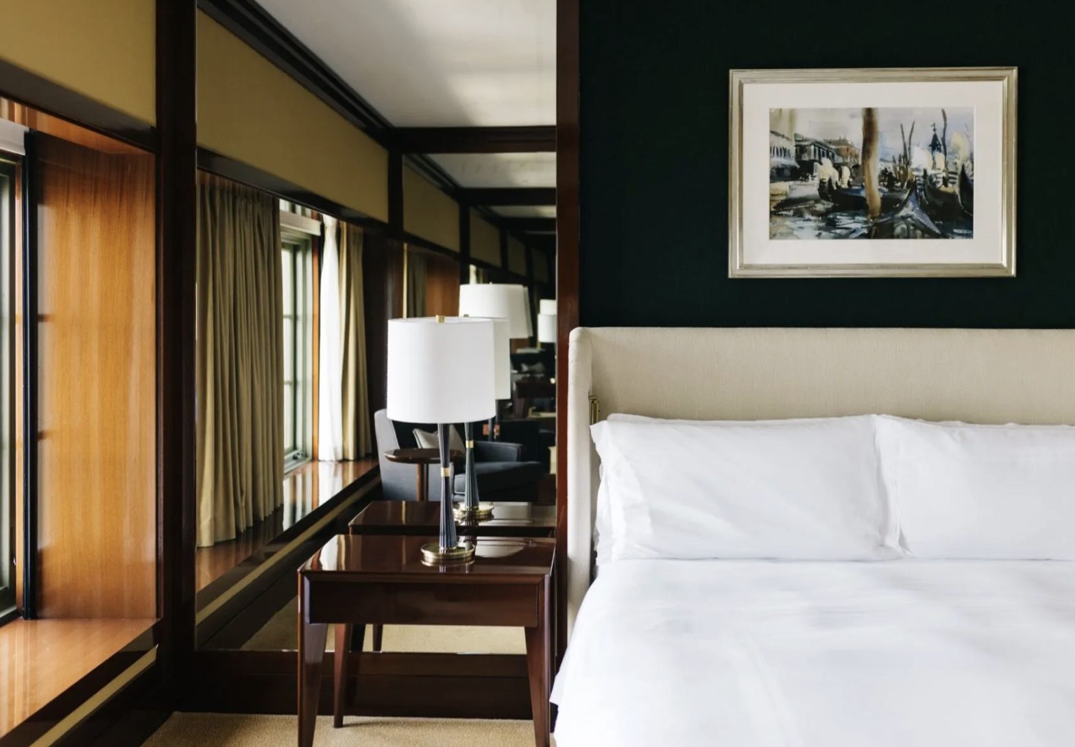 The two-bedroom suite — a serene bedroom with an upholstered headboard, deep green walls, and framed art.