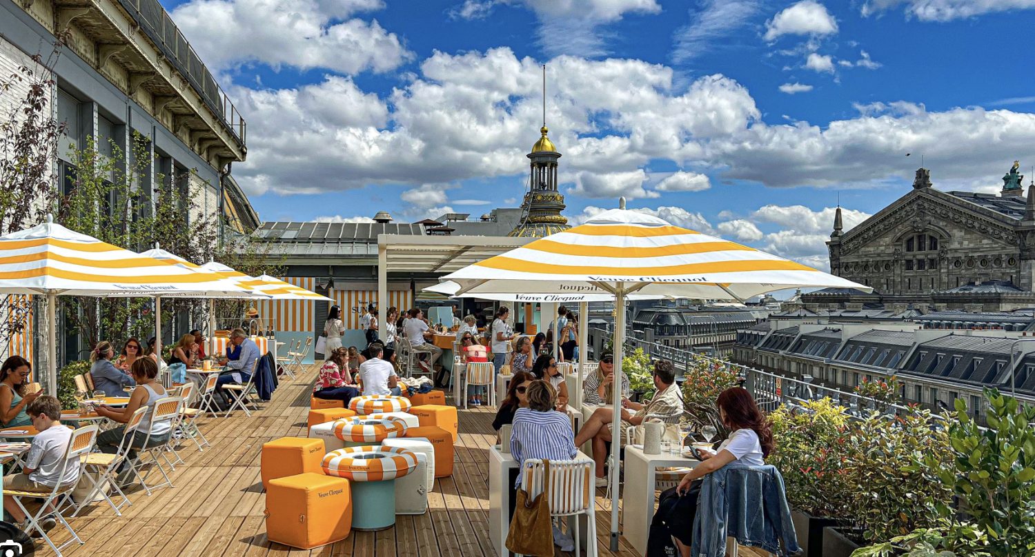 A lively rooftop party under striped umbrellas with the skyline beyond